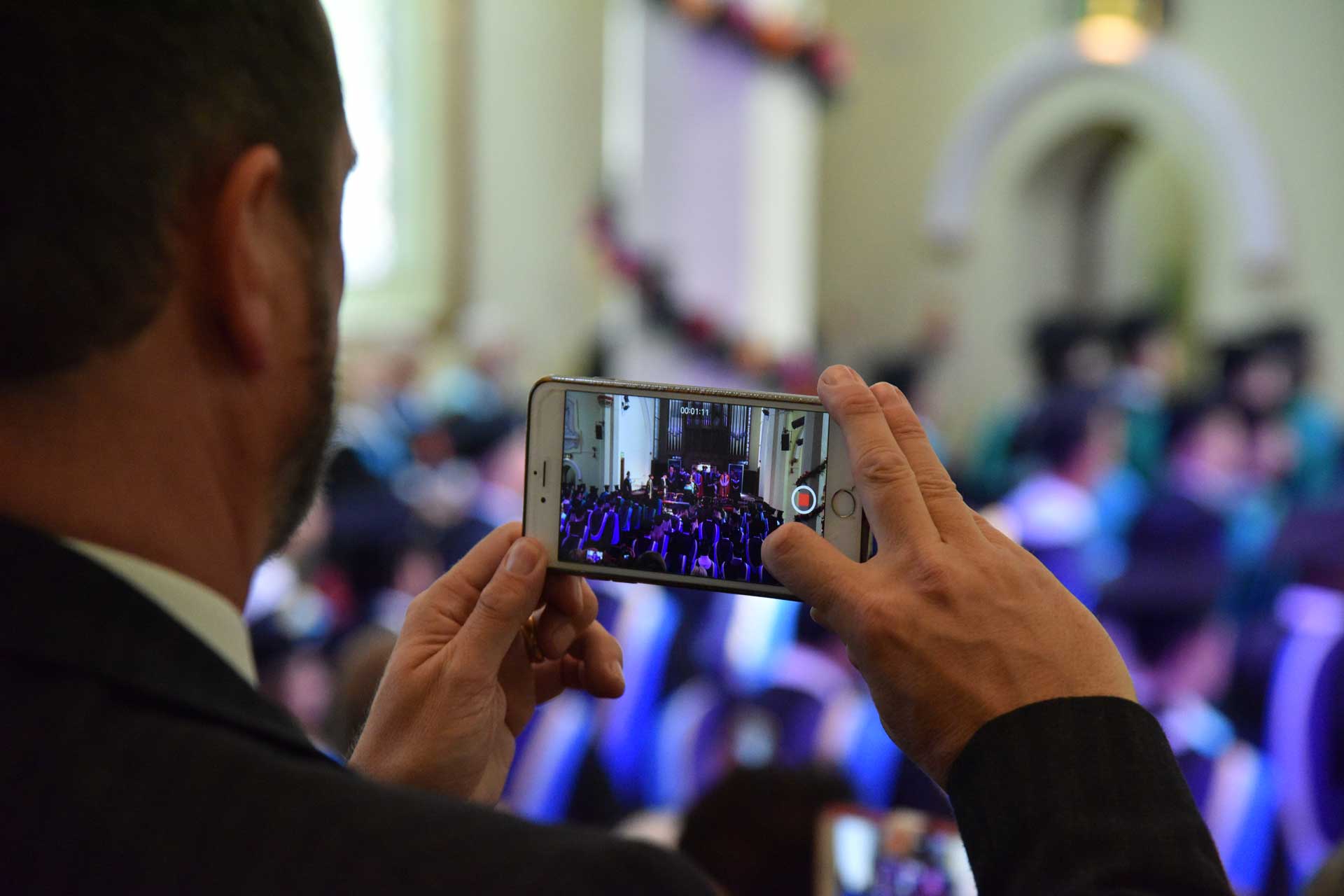 Parent taking photo on phone of group of graduates in St. Pauls