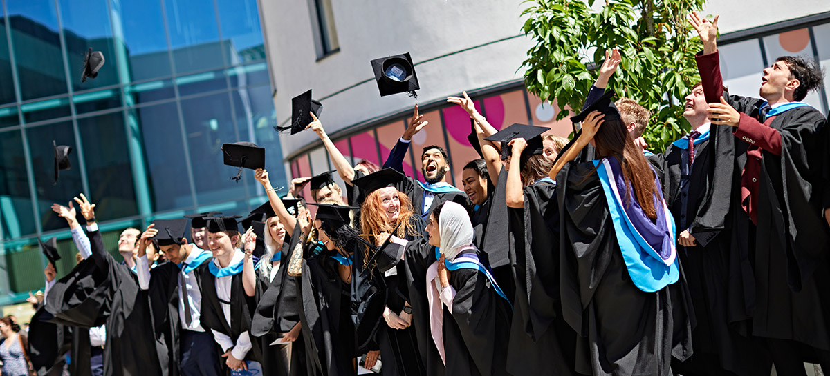 A large group of students at graduation, throwing their caps in the air and celebrating.