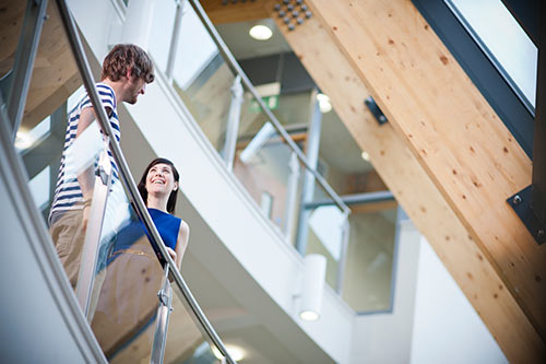 Picture of two students standing next to the glass railing in the business school.